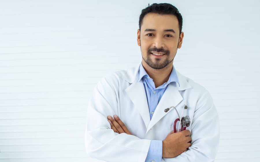 Portrait Asian handsome male doctor with beard wearing white ground uniform, holding stethoscope, smiling with kindness, happiness, posing, crossing arms with copy space. Health and Medical Concept.